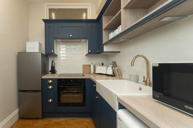 Modern kitchen with dark blue cabinetry, stainless steel appliances, white countertop and sink