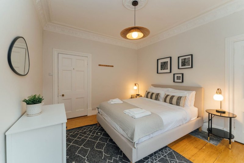 Bright modern bedroom with queen bed, pendant light, wooden floors and neutral decor