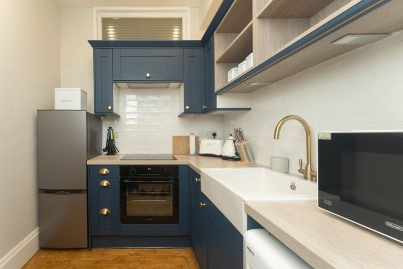 Modern kitchen with dark blue cabinetry, stainless steel appliances, white countertop and sink