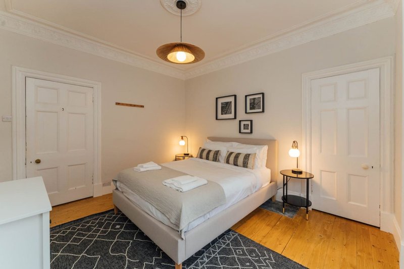 Bright bedroom with queen bed, wooden floors, pendant light, and two white doors