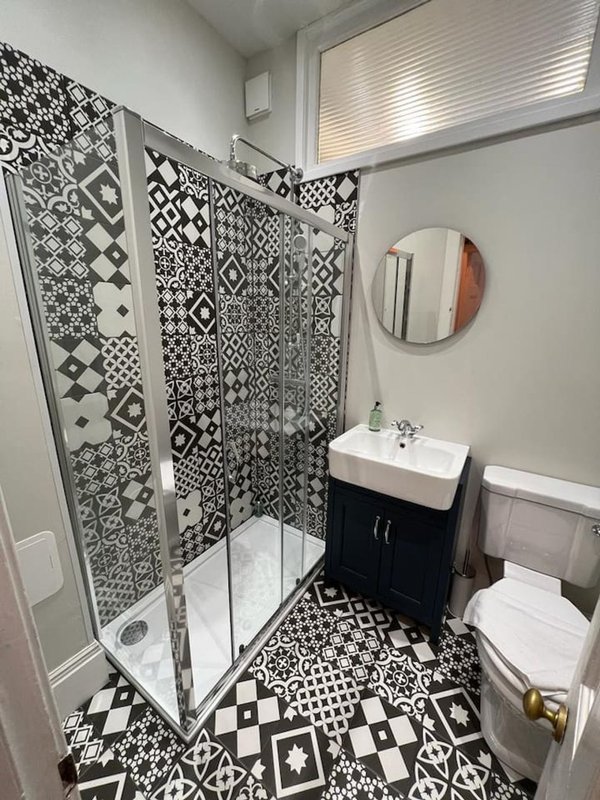 Modern bathroom with black and white patterned shower enclosure, vanity sink, toilet, and round mirror
