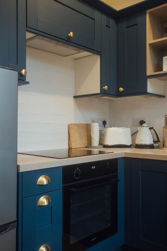 Modern kitchen with dark blue cabinetry, wooden countertop, built-in oven and kettle