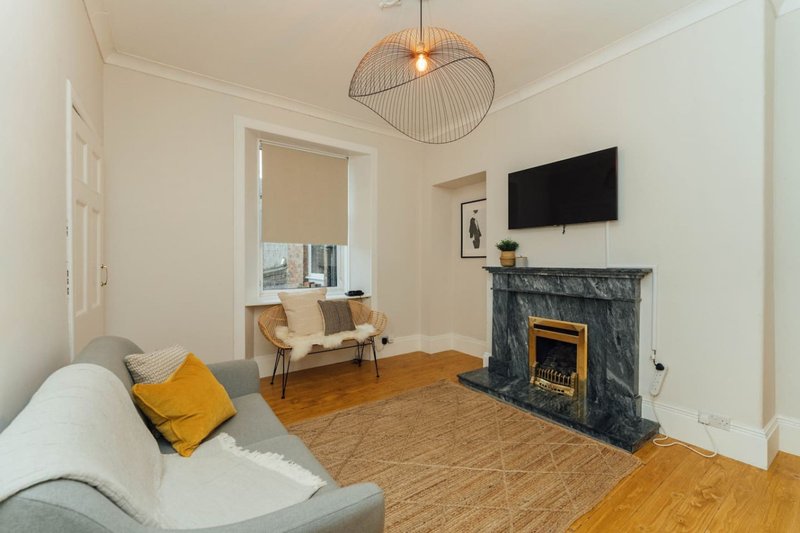 Bright living room with gray sofa, fireplace, wall-mounted TV, and wooden flooring