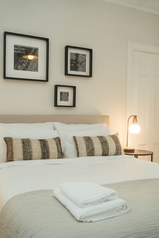 Bedroom with double bed, striped pillows, white bedding, framed wall art and pendant lamp