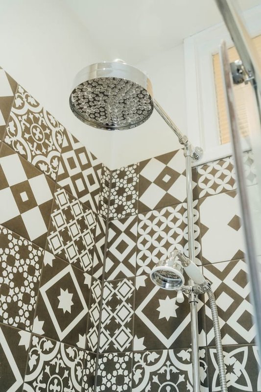 Modern bathroom shower with patterned brown and white tile walls and chrome showerhead