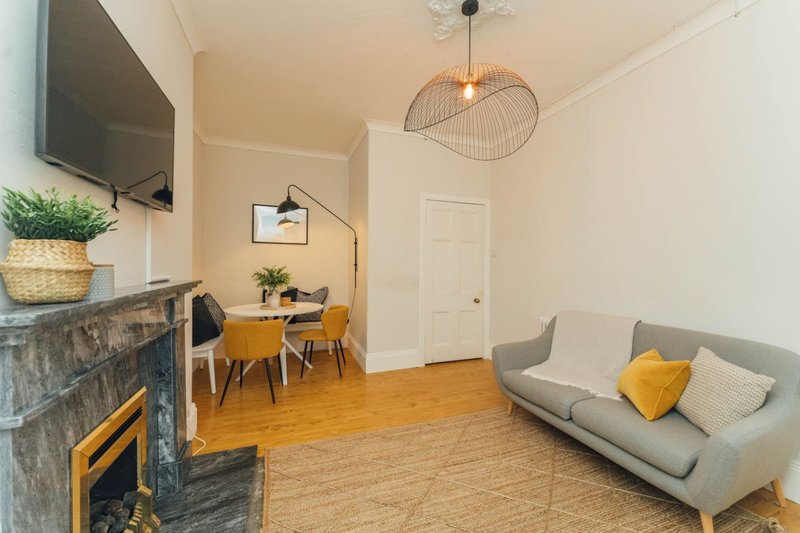 Modern living room with grey sofa, yellow accents, wooden floor and dining area