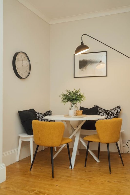 Modern dining nook with white table, yellow upholstered chairs, wall clock and framed artwork