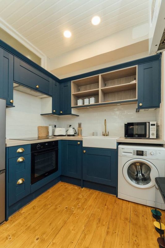 Modern kitchen with dark blue cabinetry, white appliances, open shelving and wooden flooring