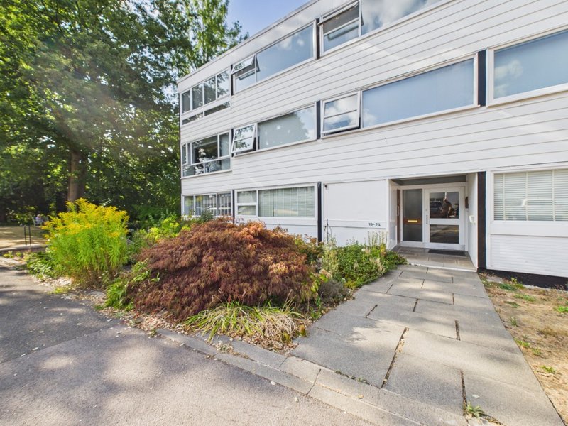 Modern white apartment building exterior with landscaped front garden and paved pathway entrance