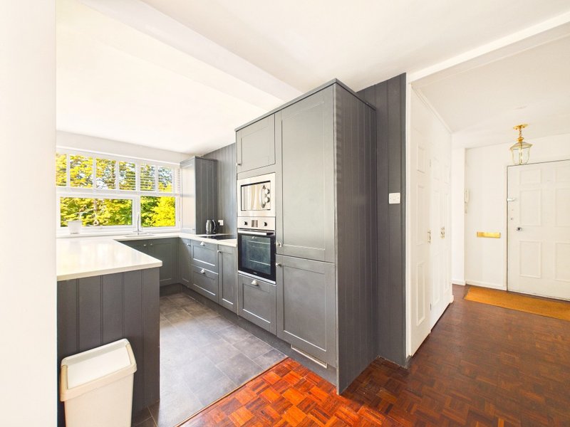 Modern kitchen with dark grey cabinetry, built-in oven, island counter and bright window overlooking garden