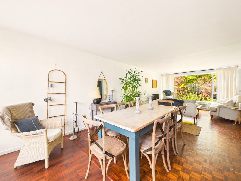 Open-plan living and dining area with wooden dining table, chairs, armchair, and garden view
