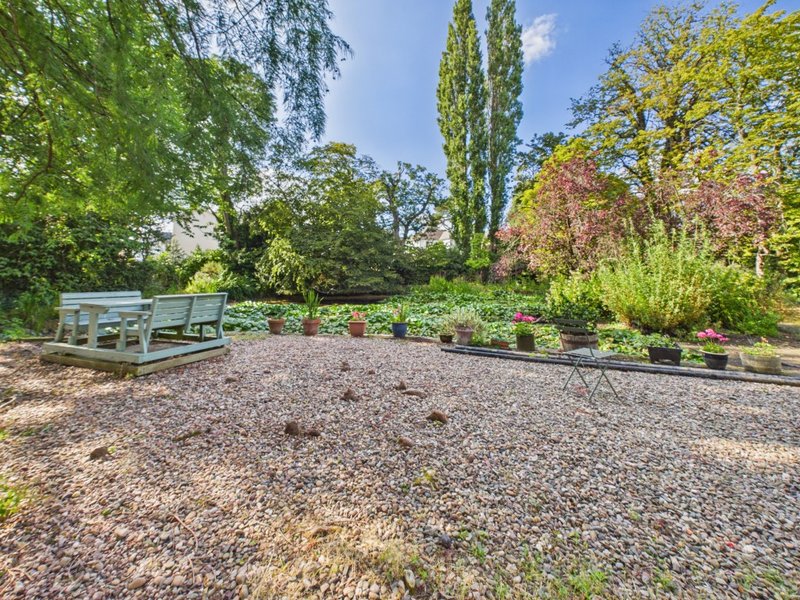 Garden area with gravel, raised beds, flowering shrubs and mature trees