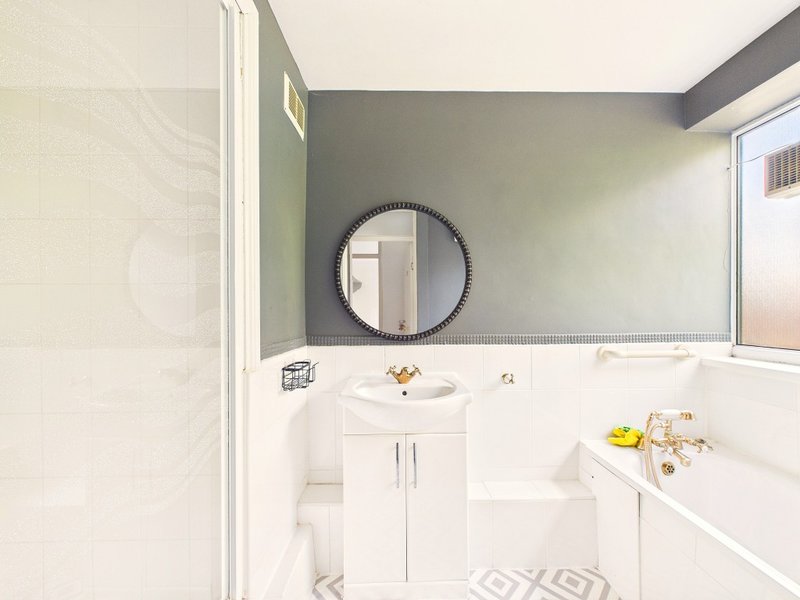 Modern bathroom with white vanity, round mirror, toilet, bathtub and grey accent wall