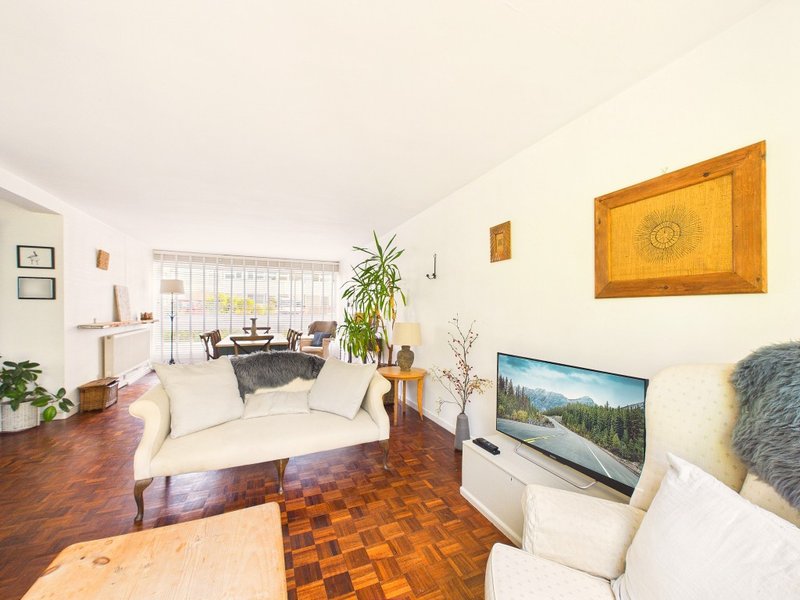 Bright living room with cream armchairs, wooden floor, plants, and wall art