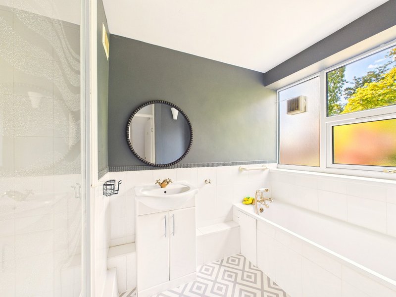 Modern bathroom with white vanity, round mirror, bathtub and window with natural light