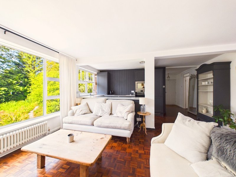 Open-plan living room with white sofas, wooden coffee table, and large window overlooking green garden