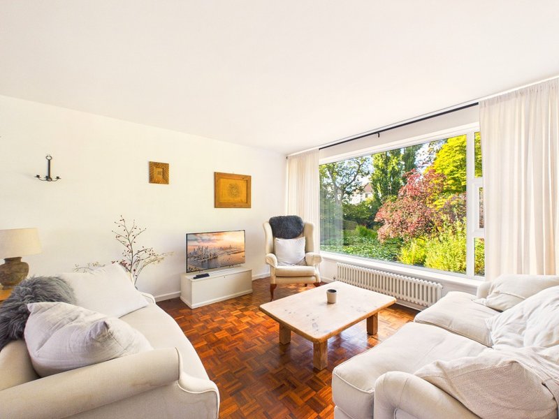 Bright living room with cream sofas, wooden coffee table, garden views through large windows