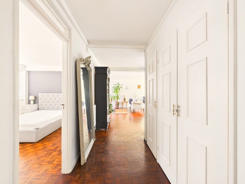 Bright hallway with wooden flooring, white doors, and view into bedroom and living area