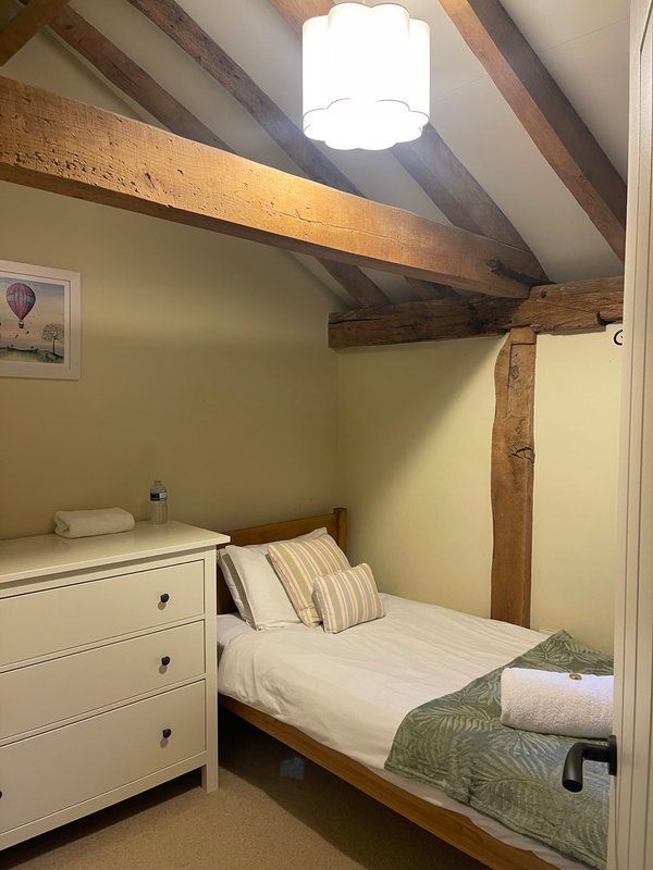 Compact bedroom with single bed, white dresser, exposed wooden beams, and skylight window