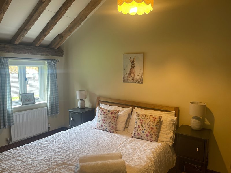 Bright bedroom with double bed, yellow walls, wooden beams, window with blue curtains