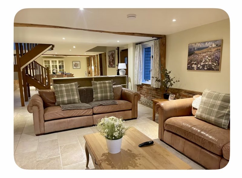 Open-plan living room with brown leather sofas, plaid cushions, wooden coffee table and staircase