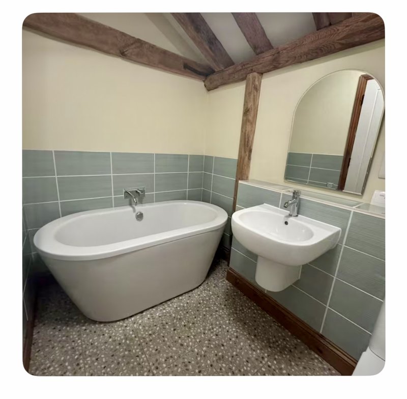 Bathroom with freestanding white bathtub, wall-mounted sink, mirror, and exposed wooden beams