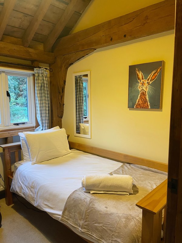Bright yellow bedroom with wooden four-poster bed, white bedding, window and framed artwork