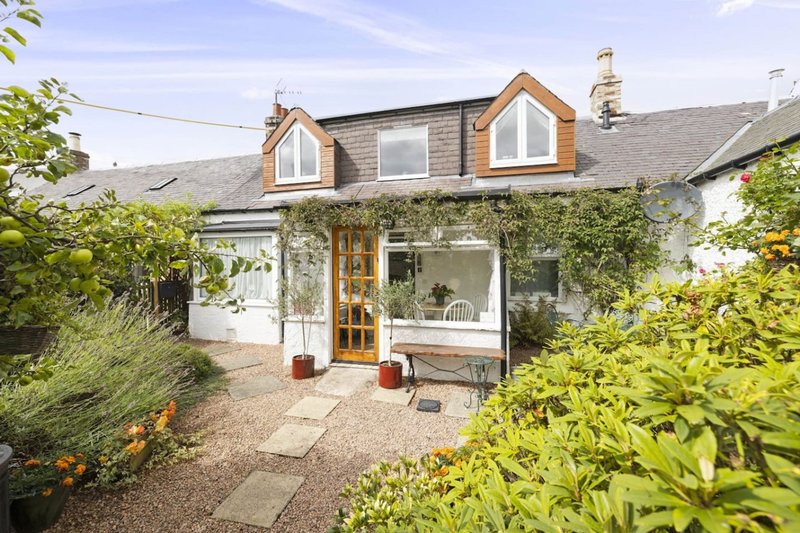 Stone cottage exterior with ivy-covered walls, modern extension, and gravel driveway
