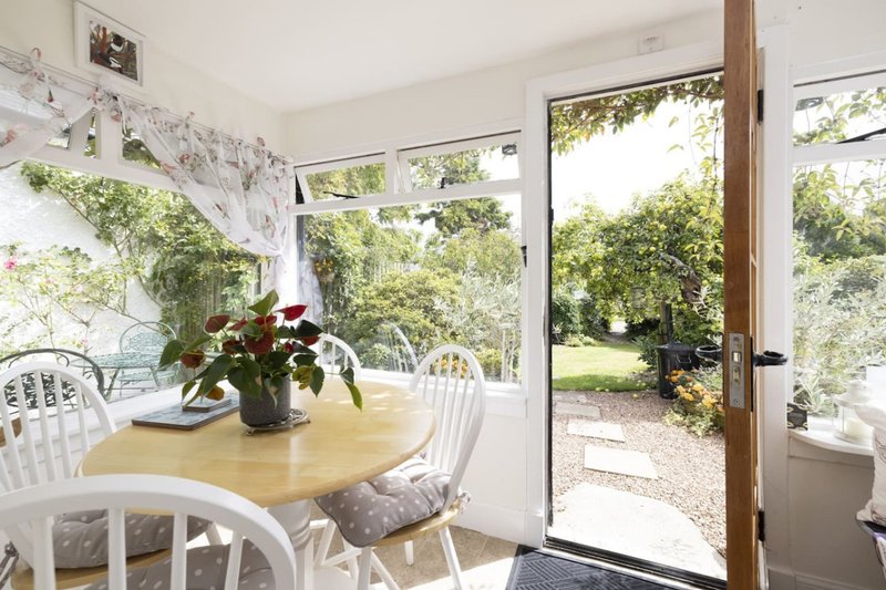 Bright dining area with round wooden table, white chairs, potted flowers and garden views through glass doors