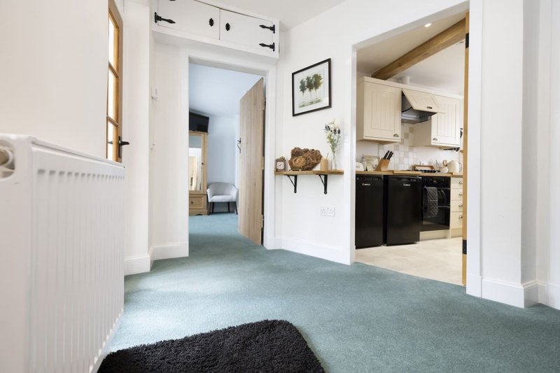 Open-plan hallway and kitchen with gray carpet, white walls, and black oven range visible