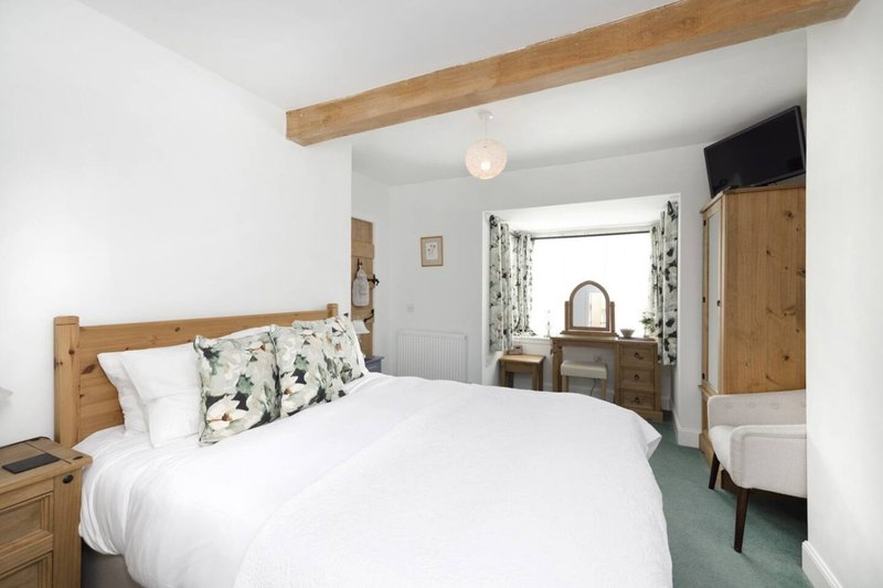 Bright bedroom with wooden bed frame, white bedding, patterned cushions, exposed beam ceiling and wooden furniture