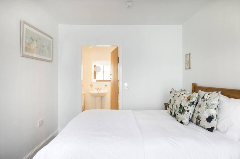 Bright bedroom with double bed, white bedding, patterned pillows, and ensuite bathroom visible through doorway