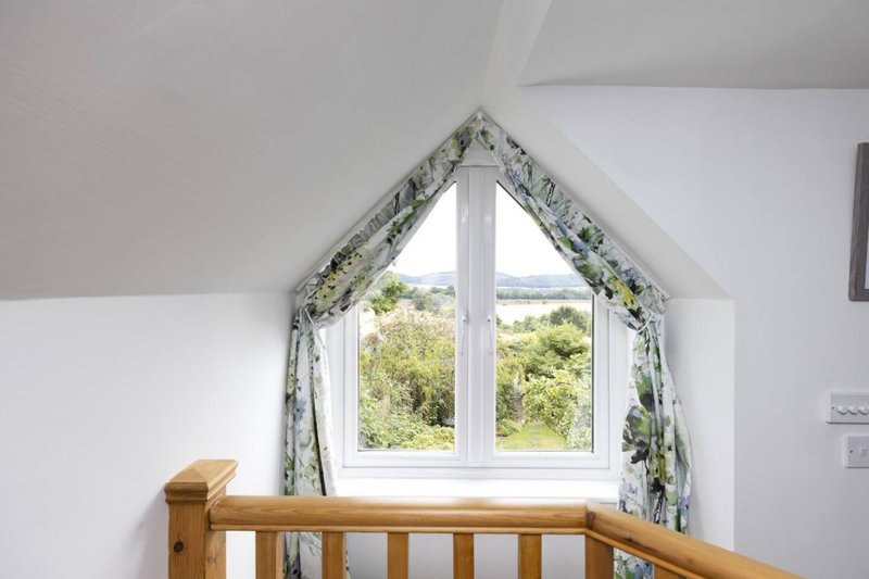Attic bedroom window with floral curtains, wooden banister, countryside views