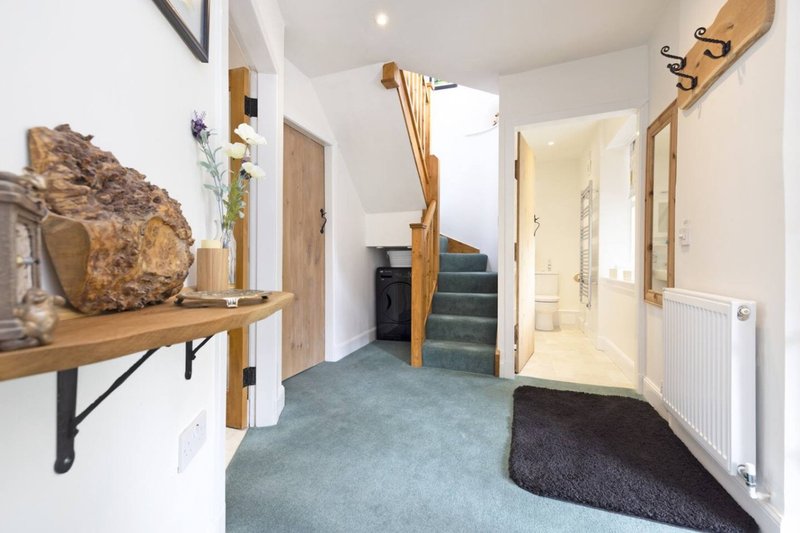 Bright hallway with wooden shelving, stairs, bathroom door, and dark entry mat