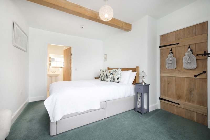 Bright bedroom with double bed, wooden beam ceiling, green carpet and wooden wardrobe
