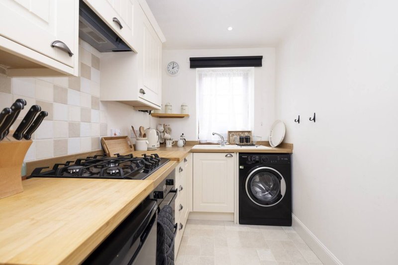 Modern kitchen with wooden countertop, gas hob, white cabinets and black washing machine