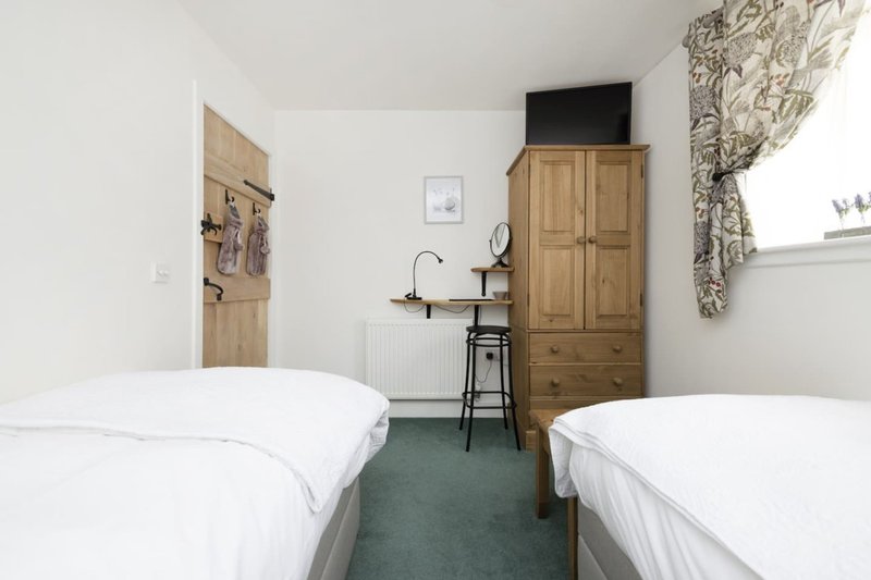 Twin bedroom with white bedding, wooden wardrobe, desk area and patterned curtains