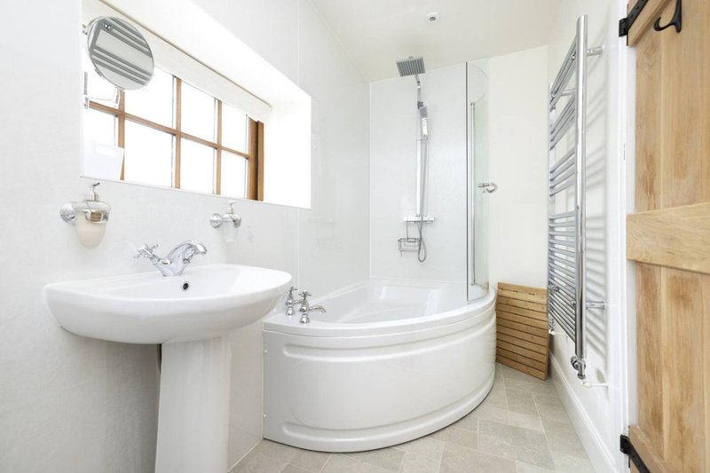 Modern bathroom with corner bathtub, pedestal sink, window and heated towel rail