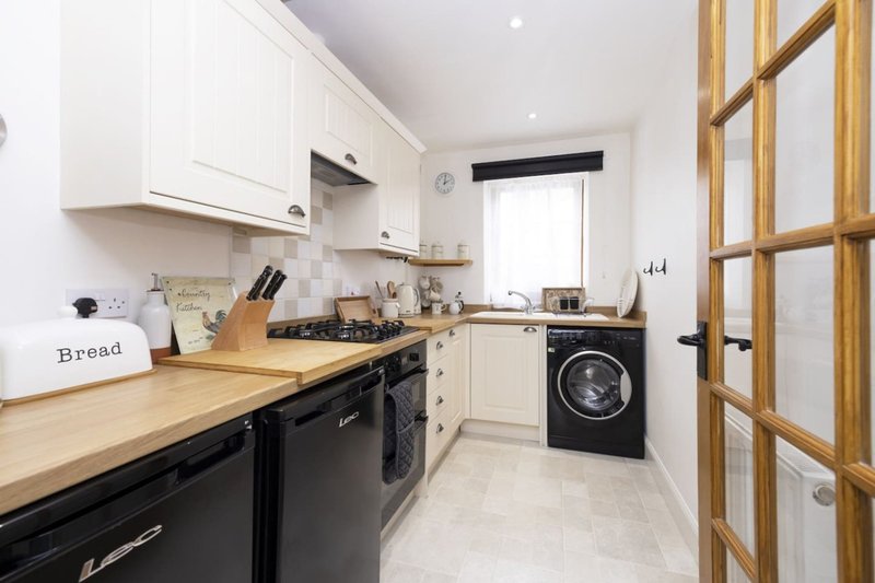 Modern kitchen with white and black cabinetry, wooden countertop, integrated appliances and washing machine