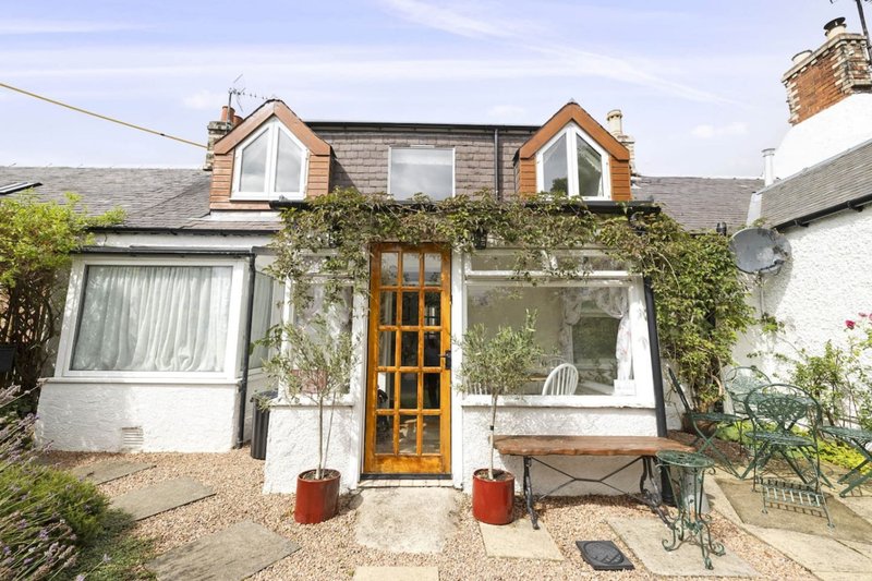 Cottage exterior with ivy-covered facade, wooden door, dormer windows and gravel driveway