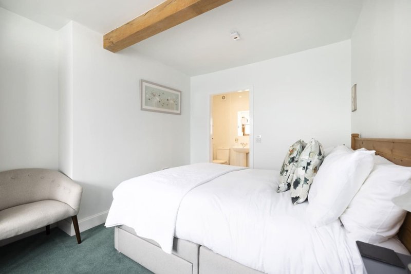 Bright bedroom with double bed, wooden beam ceiling, gray armchair and ensuite doorway
