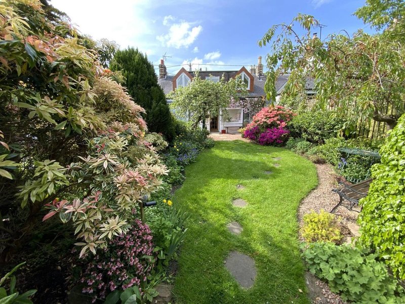 Large stone house with manicured garden, landscaped lawn, flowering shrubs and winding gravel path