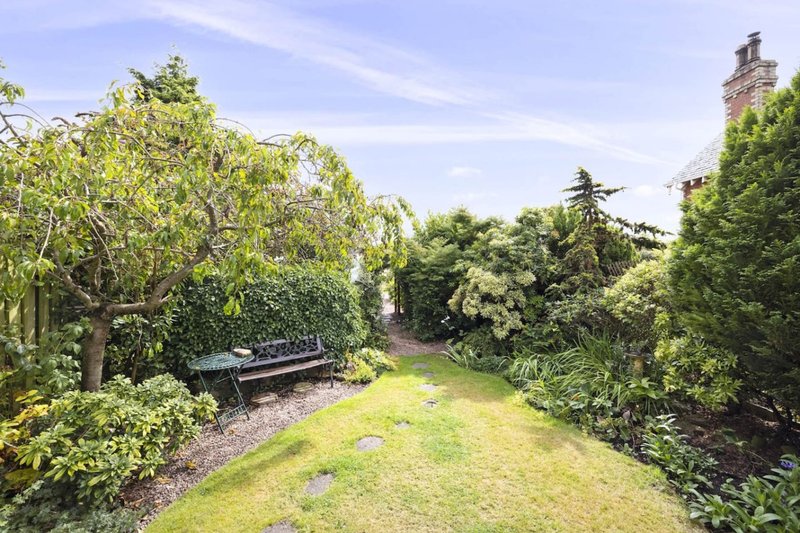 Garden view with manicured lawn, mature trees, and wooden bench seating