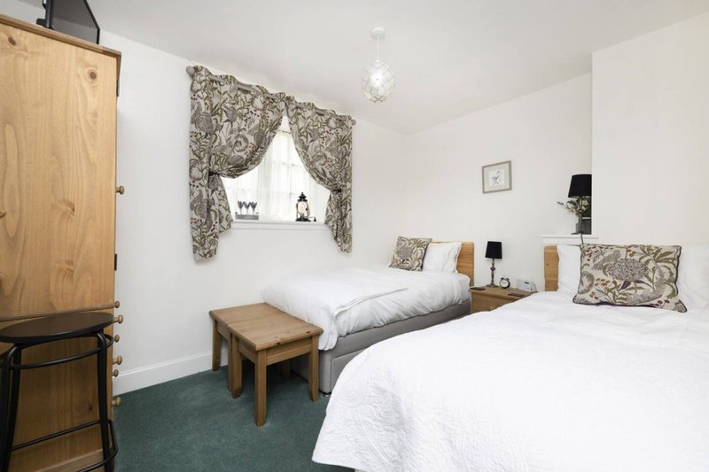 Twin bedroom with white bedding, patterned curtains, wooden furniture and green carpet