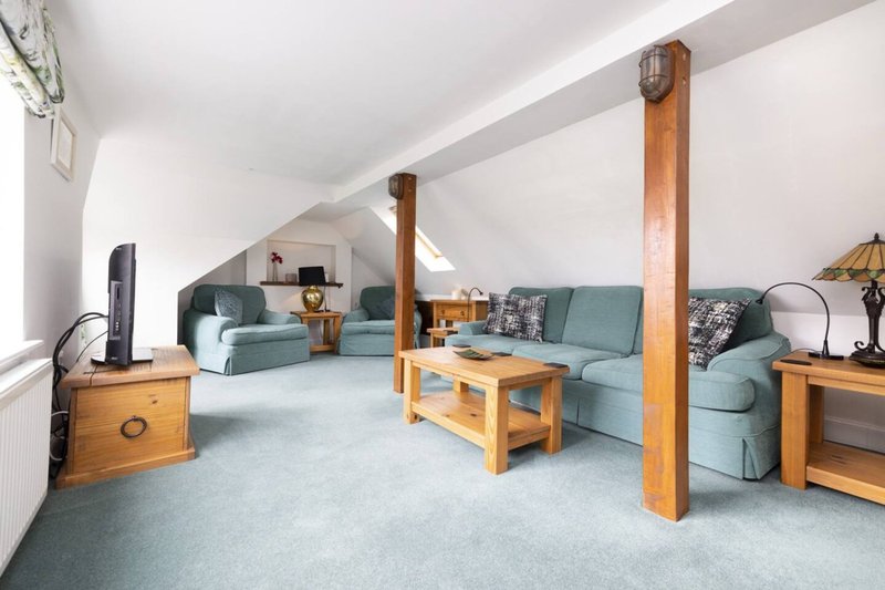 Spacious attic room with wooden beams, blue-green sofas, wooden furniture and grey carpet flooring