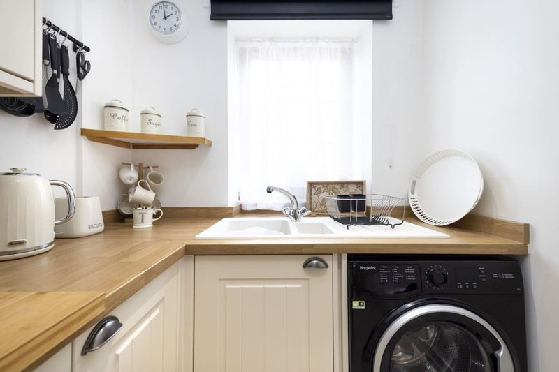 Compact kitchen with cream cabinets, wooden countertop, sink, washing machine and window