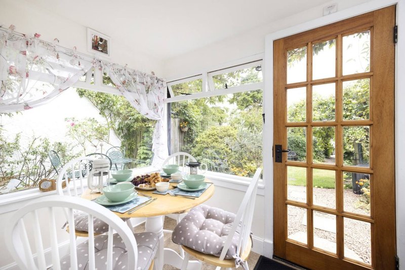 Bright dining nook with white chairs, wooden table, place settings, and garden views through French doors