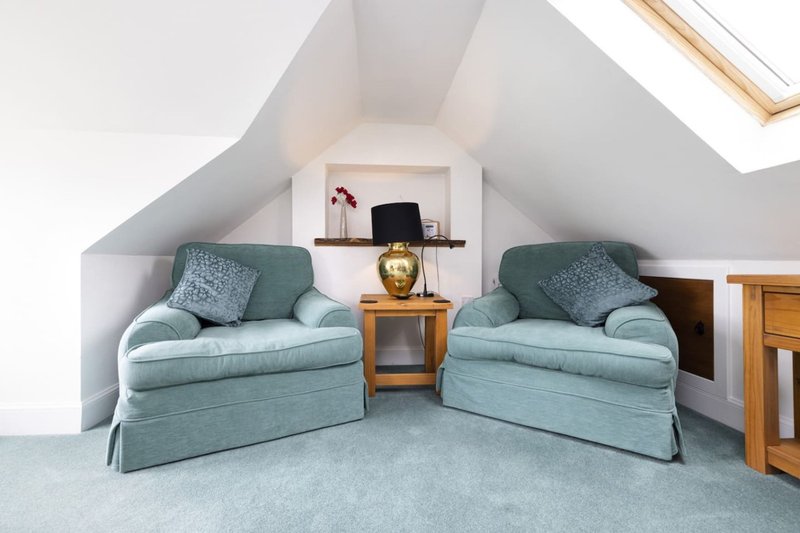 Bright attic room with two upholstered armchairs, wooden side table, skylight window