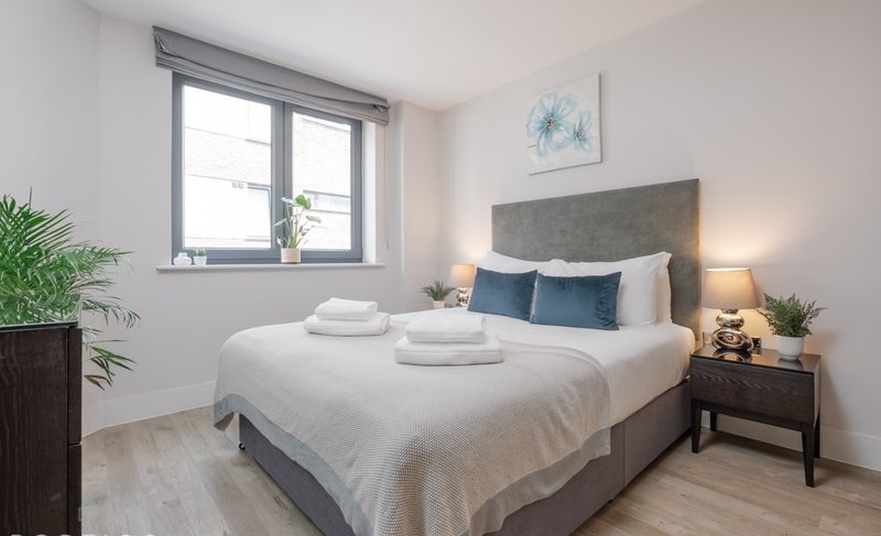 Bright bedroom with double bed, grey headboard, bedside tables and potted plants
