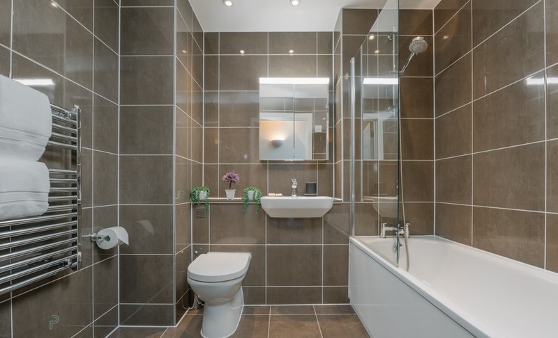 Modern bathroom with brown tile walls, white bath, toilet, sink and heated towel rail